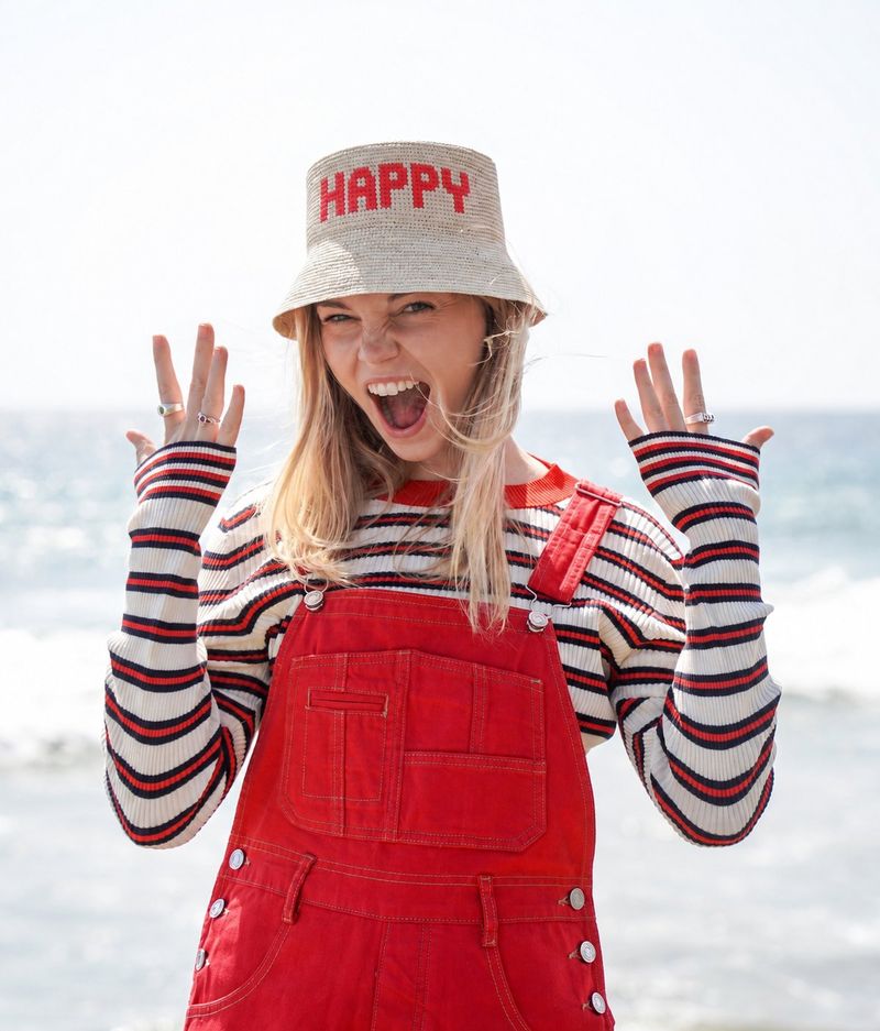 RACHOL HAPPY hat worn with red overalls at the beach